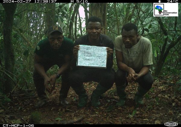 Three field team members crouching beside a camera trap with a survey identification board.