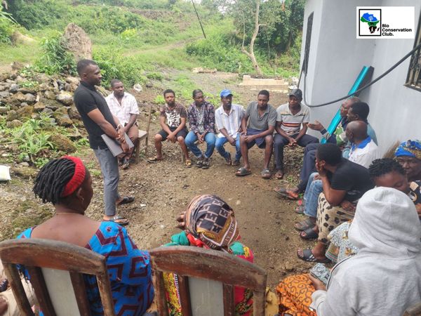 A facilitator speaking with community members seated together outdoors.