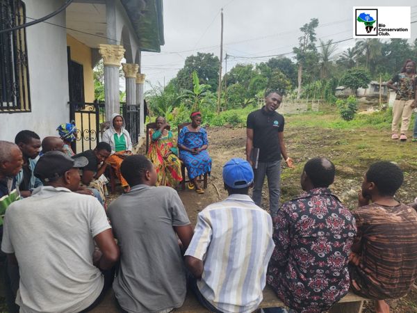 Community members listening to a facilitator at an outdoor meeting.