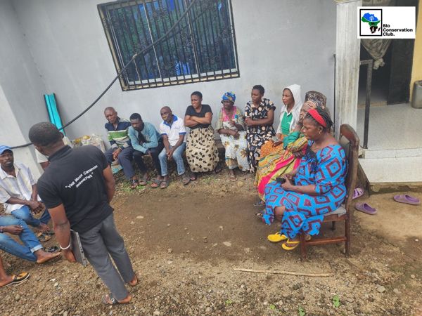 Community members seated beside a building during an outdoor discussion.