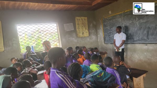 A facilitator standing at a blackboard while students listen in a classroom.