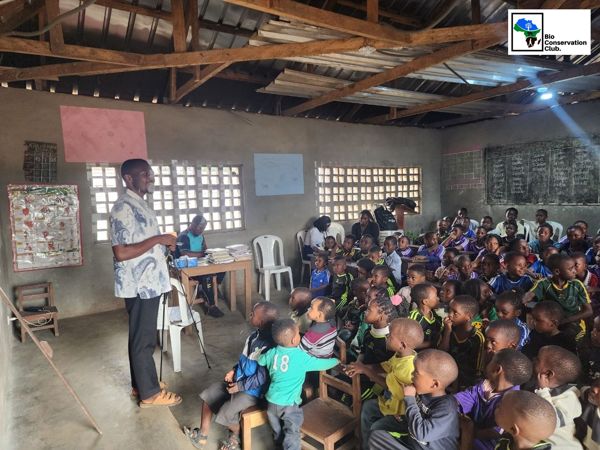 A facilitator speaking beside a tripod while students listen in a classroom.