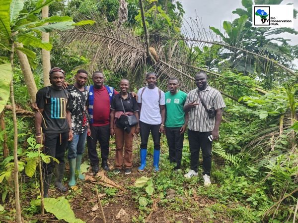 Seven field team members posing together among green forest vegetation.